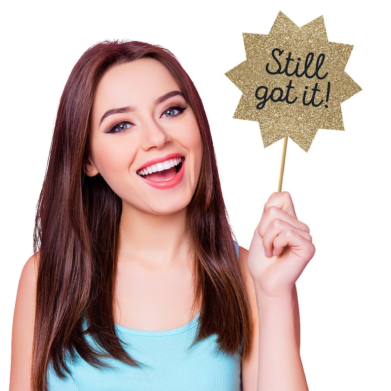 May include: A woman smiles and holds a gold glitter star-shaped sign that says "Still got it!"