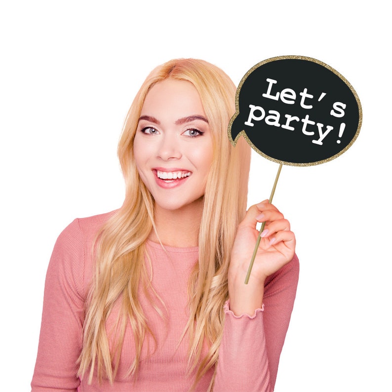 May include: A woman holds a black and gold glitter speech bubble photo booth prop that says "Let's party!"