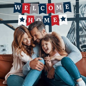 A family of three, a woman, a man, and a young girl, are sitting on a couch together. They are smiling and hugging. A banner with the words "Welcome Home" hangs above them. The banner is red, white, and blue.