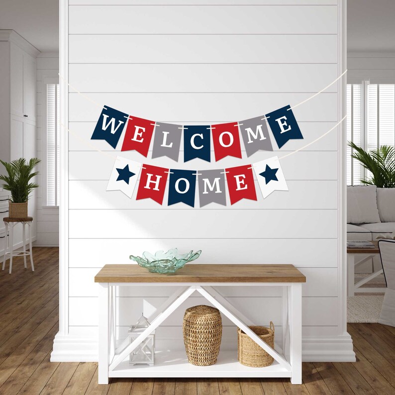 A red, white, and blue banner with the words "WELCOME HOME" hanging on a white wall. The banner is made of felt and has stars on each end.