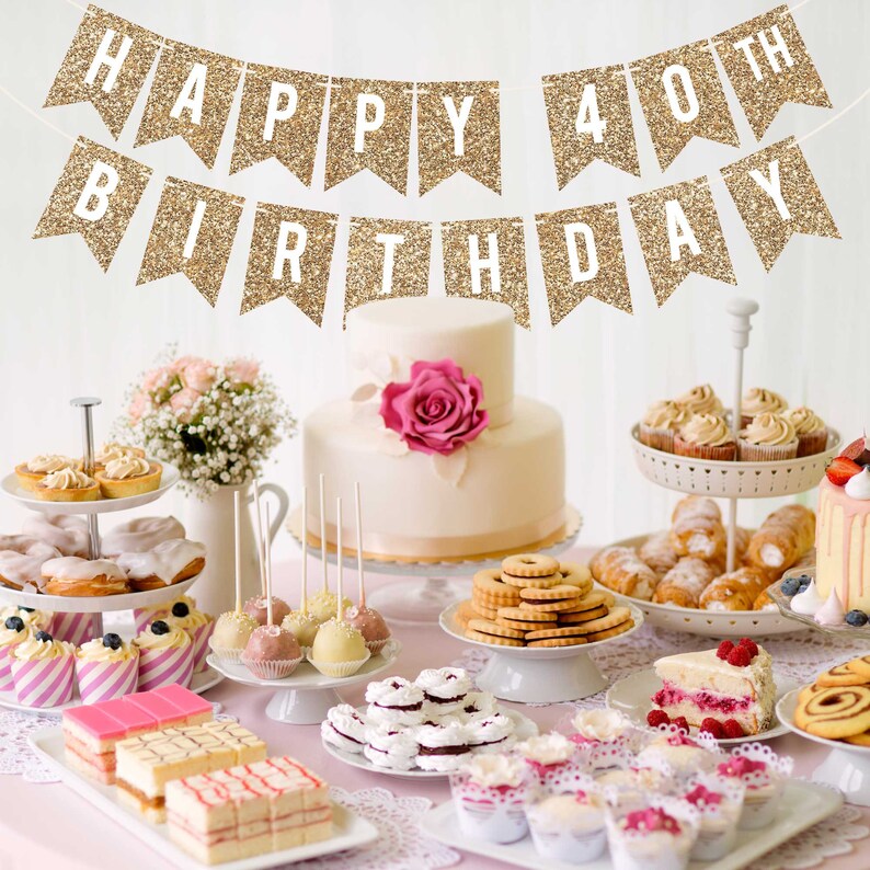 A gold glitter banner with the text "Happy 40th Birthday" hangs above a table with a variety of desserts, including cupcakes, cake pops, and a two-tiered cake.