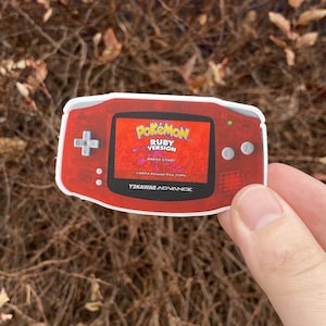 May include: Red and white Game Boy Advance SP sticker with a screen displaying the Pokemon Ruby Version start screen. The screen reads "Pokemon Ruby Version" and "Press Start".