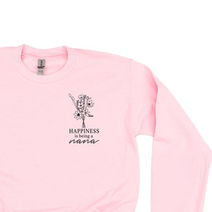 Op de afbeelding: Roze sweatshirt met een bloemenontwerp en de tekst "Happiness is being a nana" op de voorkant.