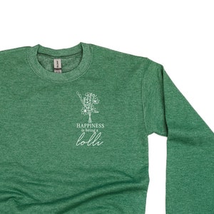 Könnte beinhalten: Ein grüner Pullover mit einer weißen Grafik, auf der "Happiness is being a lolli" steht, und einem kleinen Blumenmuster.