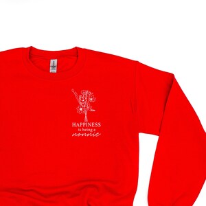 Könnte beinhalten: Roter Pullover mit einem weißen Grafikdesign, auf dem "Happiness is being a nonnie" steht, mit einem floralen Design über dem Text.