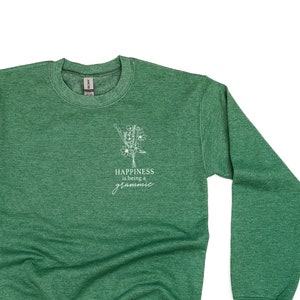 Op de afbeelding: Groen sweatshirt met een wit bloemenontwerp en de tekst "Happiness is being a gramma" op de voorkant.