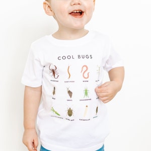 May include: White t-shirt with a graphic of different bugs and the text "COOL BUGS". The bugs include a scorpion, centipede, worm, stick bug, wasp, snail, grasshopper, praying mantis, stink bug, caterpillar, and cricket.