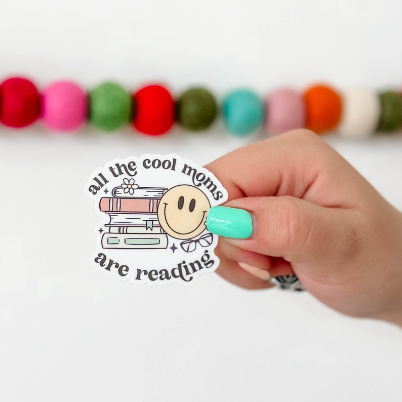 May include: A white sticker with a stack of books, a smiley face, and the text "all the cool moms are reading".