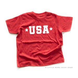 May include: Red t-shirt with white stars and the word "USA" printed on the front.