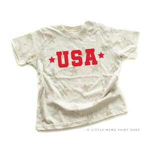 May include: A white t-shirt with a star pattern and the word "USA" in red letters.