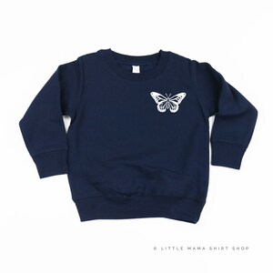 Pu&ograve; includere: Felpa a maniche lunghe blu navy con una grafica di farfalla bianca sul davanti.