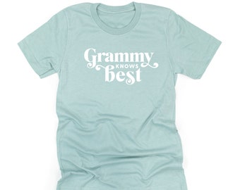 Könnte beinhalten: Ein hellblaues T-Shirt mit kurzen Ärmeln und dem weißen Schriftzug "Grammy KNOWS best" in einer stilisierten Schriftart auf der Brust. Das Kleidungsstück hat einen Rundhalsausschnitt und eine melierte Textur. Unten steht "LITTLE MAMA SHIRT SHOP".