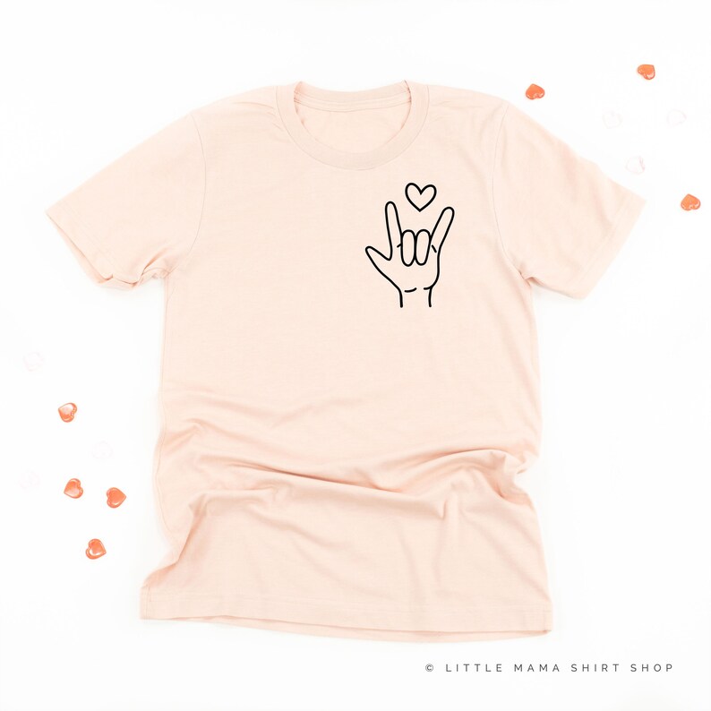 May include: A light pink t-shirt with a black graphic of a hand making the sign for 'I love you' in American Sign Language. A small heart is above the hand.