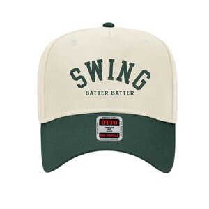 May include: A cream colored baseball cap with a green brim. The front of the cap has the word "SWING" in green letters with the words "BATTER BATTER" underneath. The back of the cap has a black and red label with the word "OTTO" in red letters.