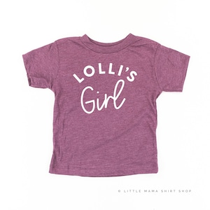 May include: A purple short-sleeved t-shirt with the text "Lolli's Girl" in white.