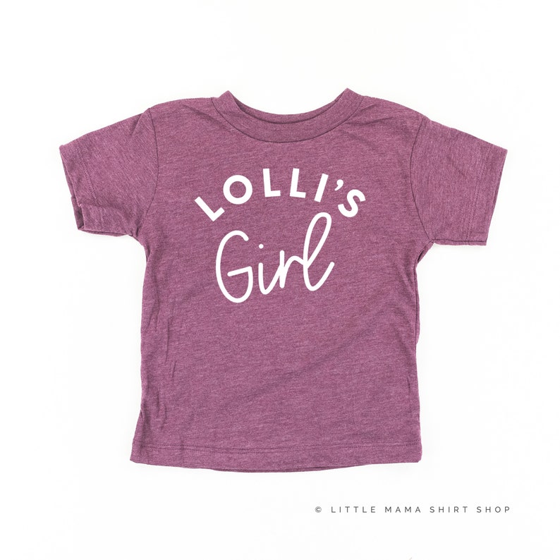 May include: A purple short-sleeved t-shirt with the text "Lolli's Girl" in white.
