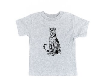 May include: A heather gray short-sleeved t-shirt featuring a black graphic illustration of a seated leopard in the center. The leopard is depicted in a realistic style with detailed spots and a long tail. The text Little Mama Shirt Shop is visible.