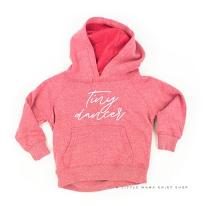 May include: A red hooded sweatshirt with the text "tiny dancer" in white lettering on the front.