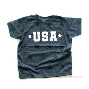 May include: A dark blue t-shirt with a white star pattern and the word "USA" in white letters.