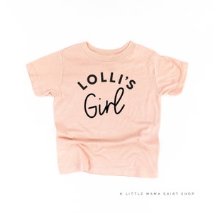 May include: A peach-colored t-shirt with black text that reads "Lolli's Girl".