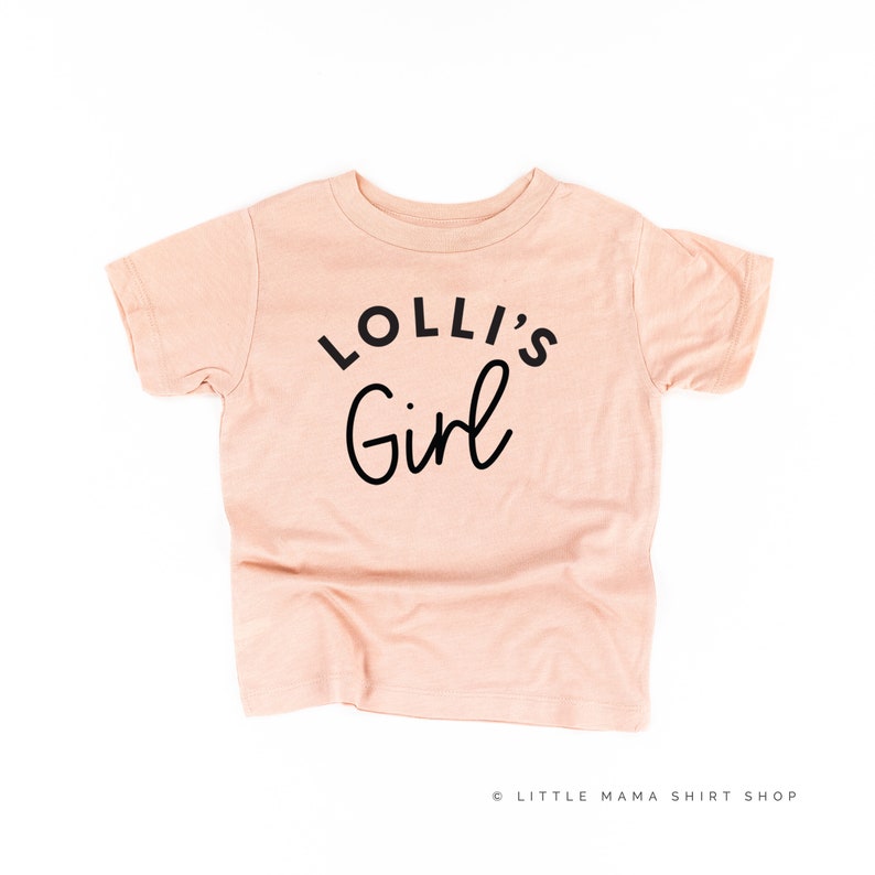 May include: A peach-colored t-shirt with black text that reads "Lolli's Girl".