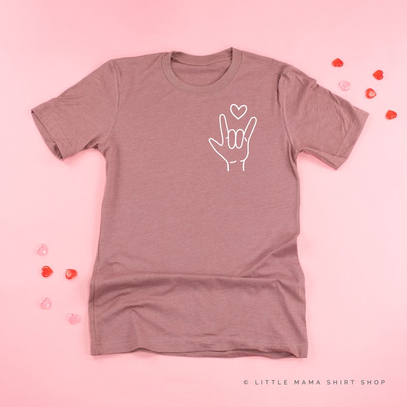 May include: A mauve colored t-shirt with a white outline of the American Sign Language symbol for "I love you" with a small heart above the hand.