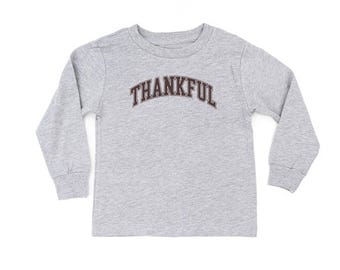 May include: A gray long-sleeved shirt with the word "THANKFUL" arched across the chest in a dark brown, collegiate-style font. The shirt is made of a soft material and has a crew neck.