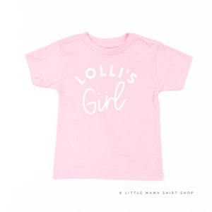 May include: Pink short-sleeved t-shirt with white text that reads "Lolli's Girl".