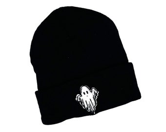 Op de afbeelding: Een zwarte beanie-muts met een wit geborduurd spookontwerp aan de voorkant. De muts is gemaakt van een zacht, gebreid materiaal en heeft een omgeslagen rand. Het spookontwerp is een eenvoudige, cartoonachtige illustratie.