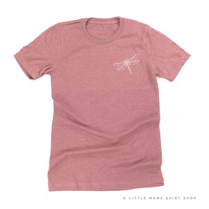 Op de afbeelding: Een stoffig roze t-shirt met een witte libel-omtrek op de linkerbovenborst. Het shirt heeft korte mouwen en een ronde hals. De tekst "LITTLE MAMA SHIRT SHOP" staat rechtsonder.