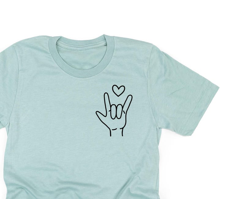 May include: A light blue t-shirt with a black outline of an ASL sign for "I love you" and a small heart above it.