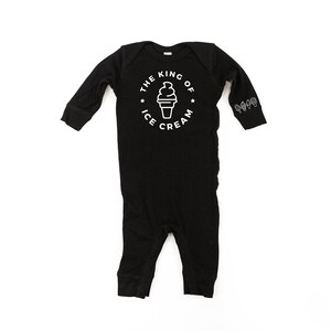 May include: Black long-sleeve baby onesie with white text that reads "The King of Ice Cream" and a graphic of an ice cream cone. The onesie has small ice cream cone graphics on the sleeves.