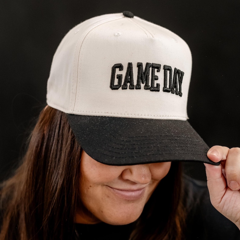 May include: A white and black baseball cap with the text "GAME DAY" embroidered in black on the front.
