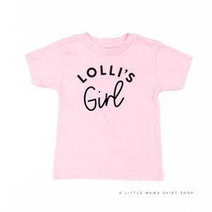 May include: Pink short-sleeved t-shirt with black text that reads "Lolli's Girl".