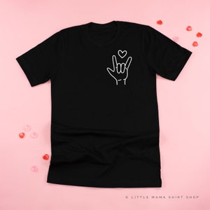 May include: Black t-shirt with a white outline of a hand making the sign for "I love you" in American Sign Language. A small heart is above the hand.