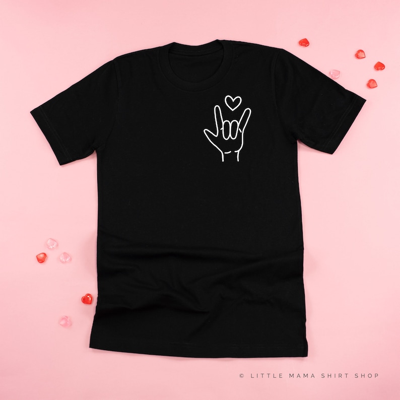 May include: Black t-shirt with a white outline of a hand making the sign for "I love you" in American Sign Language. A small heart is above the hand.