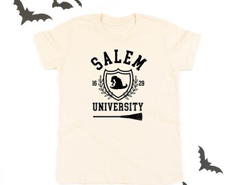 Könnte beinhalten: Cremefarbenes T-Shirt mit schwarzem Salem University-Wappen. Das Wappen zeigt einen Hexenhut, den Text "SALEM UNIVERSITY" und die Jahreszahlen "16" und "29". Unter dem Wappen befindet sich ein Besen. Dekorative Fledermaus-Ausschnitte im Hintergrund.