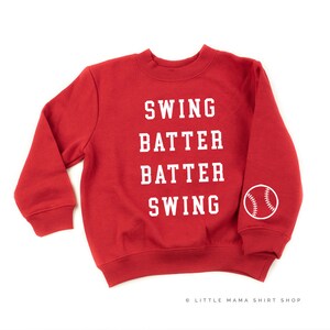 May include: Red sweatshirt with white text that reads "Swing Batter Batter Swing" and a white baseball graphic on the sleeve.