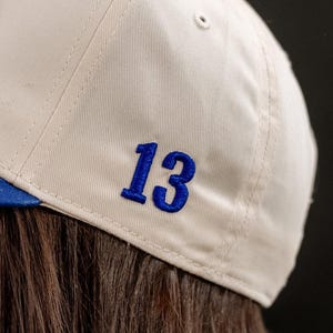 May include: A white baseball cap with a blue number 13 embroidered on the back.