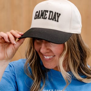 May include: A white and black baseball cap with the text "GAME DAY" in black embroidered letters.