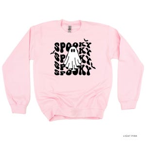 May include: Light pink crewneck sweatshirt with a black graphic of a ghost and the word "Spooky" repeated. The design includes bats. The sweatshirt is a solid light pink color.