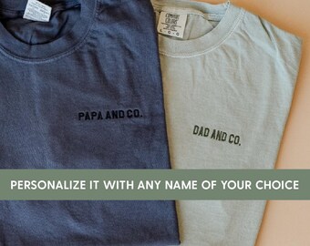 May include: Two Comfort Colors t-shirts, one navy blue and one sage green, with the phrases "PAPA AND CO." and "DAD AND CO." embroidered on the front. The image includes the text "PERSONALIZE IT WITH ANY NAME OF YOUR CHOICE."