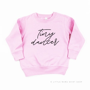 May include: Pink long-sleeved sweatshirt with the text "Tiny dancer" in black script.
