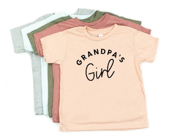 May include: A peach-colored t-shirt with short sleeves and a black graphic that says "Grandpa's Girl".