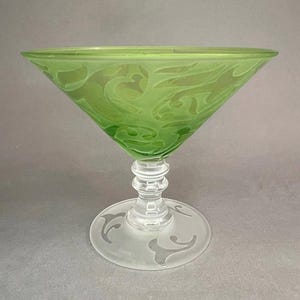 May include: A green glass martini glass with etched floral designs. The bowl is triangular, and the stem is clear with a decorative base. The base of the glass has etched floral designs.