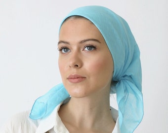 Op de afbeelding: Een vrouw draagt een lichtblauwe hoofddoek en een wit overhemd met knopen en een gouden ketting.