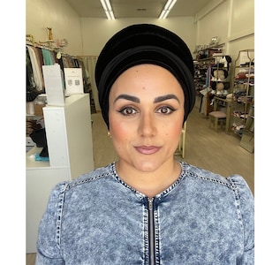 May include: A black velvet turban with a simple design. The turban is worn by a person with a denim jacket.