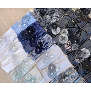 Może przedstawiać: Zestaw opaski do włosów z tkaniny w różnych odcieniach niebieskiego i szarego. Opaski ozdobione są dużymi, warstwowymi rozetkami z tkaniny.