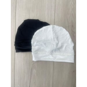 Könnte beinhalten: Zwei Stoffhauben, eine schwarze und eine weiße. Beide sind aus einem weichen, dehnbaren Material.