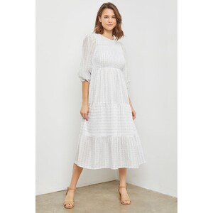 May include: A white midi dress with a floral pattern and a tiered skirt. The dress has a round neckline and 3/4 sleeves.